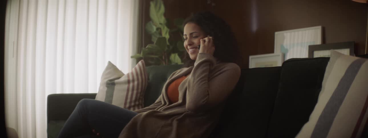 The woman talks on her phone on the couch