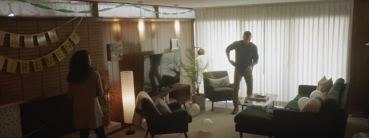 Man stands in living room with woman, looks at watch, and leaves