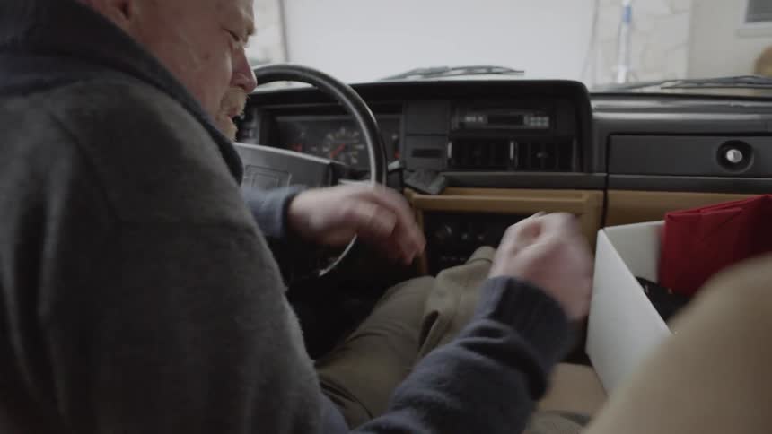 An elderly man grabs a box from the passenger seat