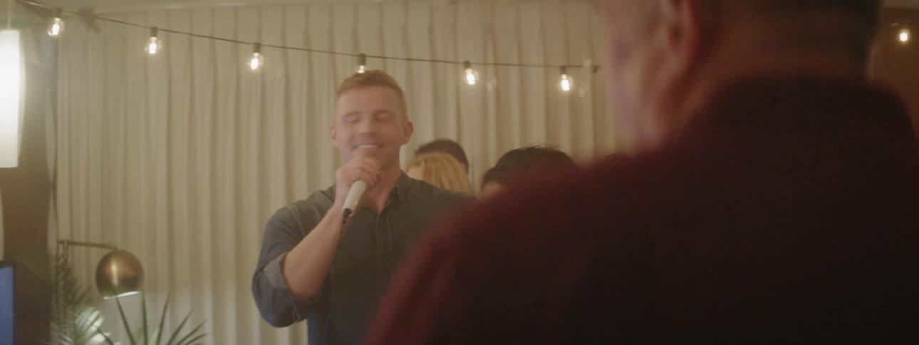 Man and woman sing into a microphone at a party