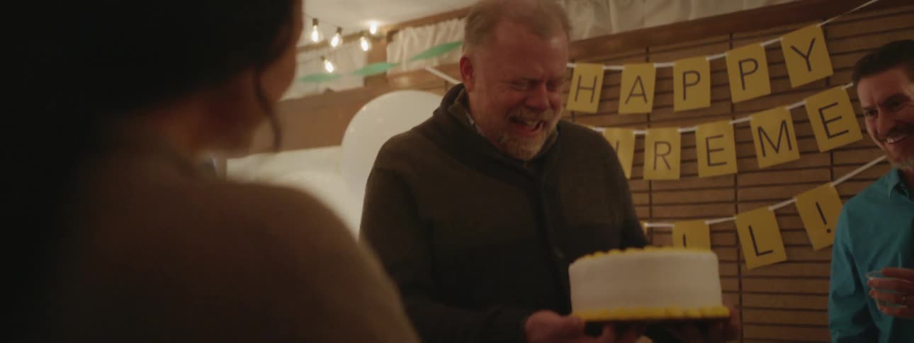 Man smiles while holding a cake at a retirement party