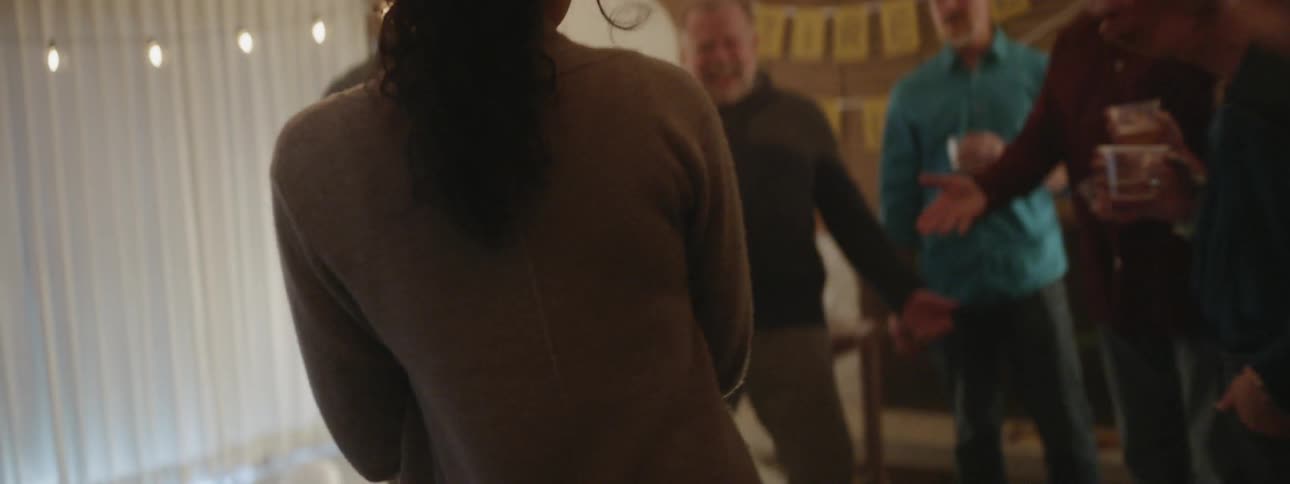 Woman carries a cake into a room and hands it to a man