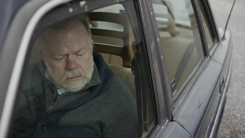 A man looks down in his car waiting