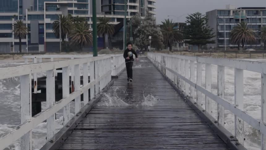 Boy runs from crashing waves on a pier