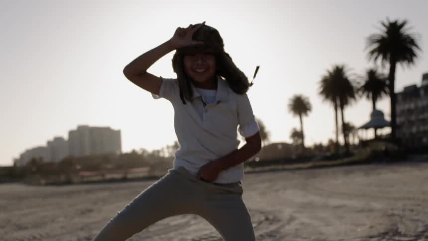 Young boy wearing a hat with ear flaps jumps up and down with his hand at his head