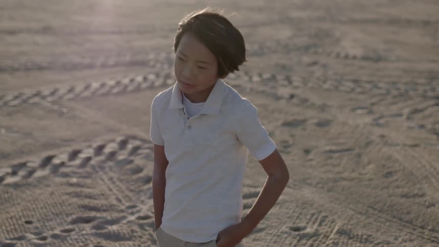 Boy stands in a dirt field at sunset