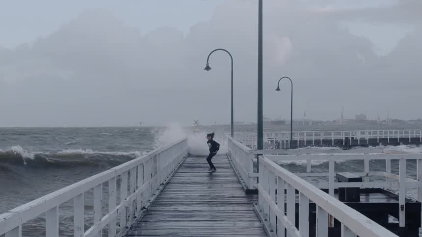 Boy hops and runs on an ocean pier near crashing waves