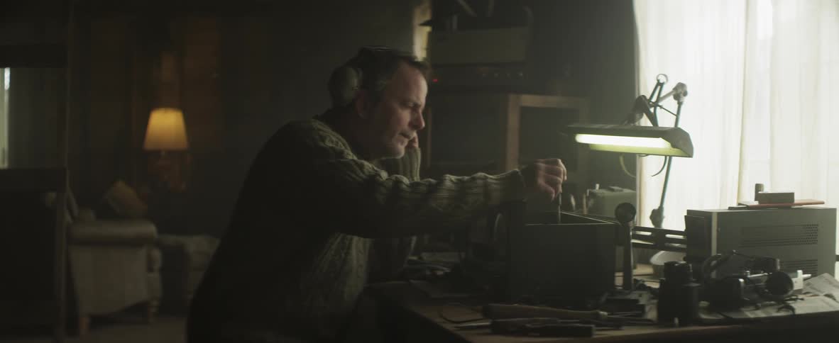 A man sits at a desk and puts on headphones