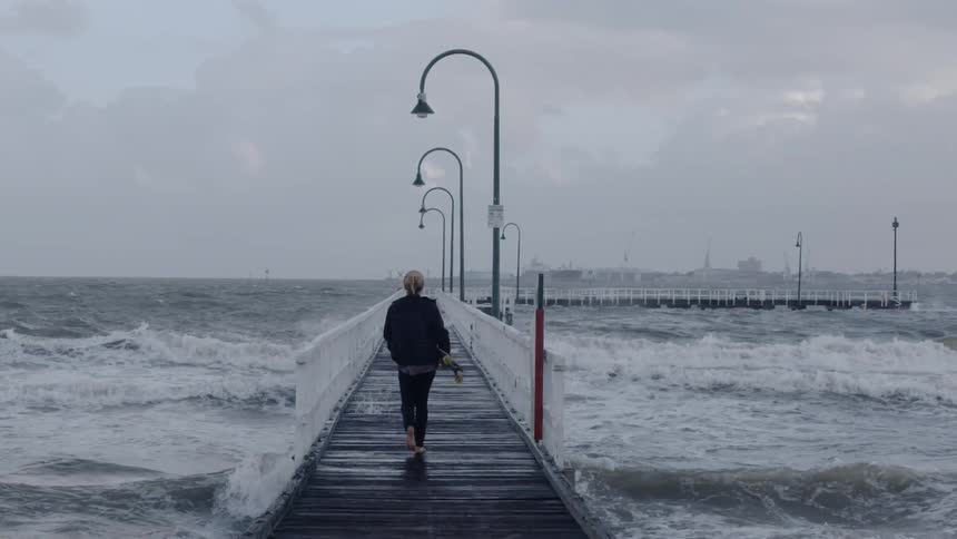 A woman walks on the pier as waves crash