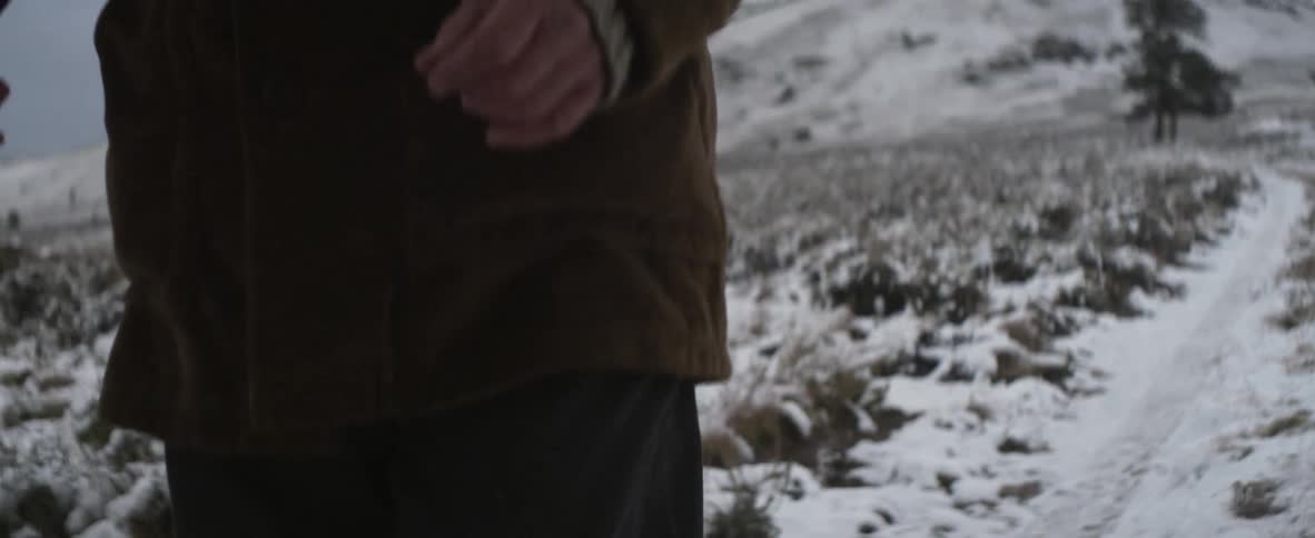View of persons hands and legs as they walk over a snowy terrain