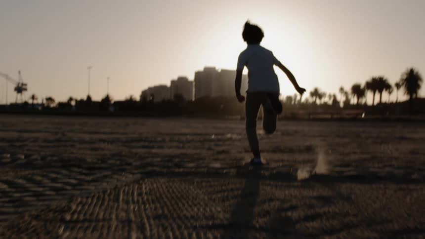 A boy runs on the sand at sunset