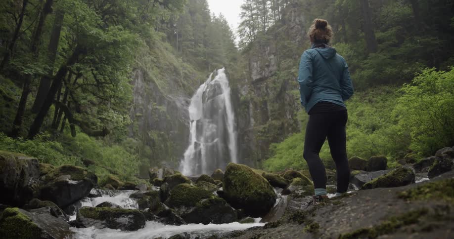 A woman watches the waterfall in a forest on a cloudy day