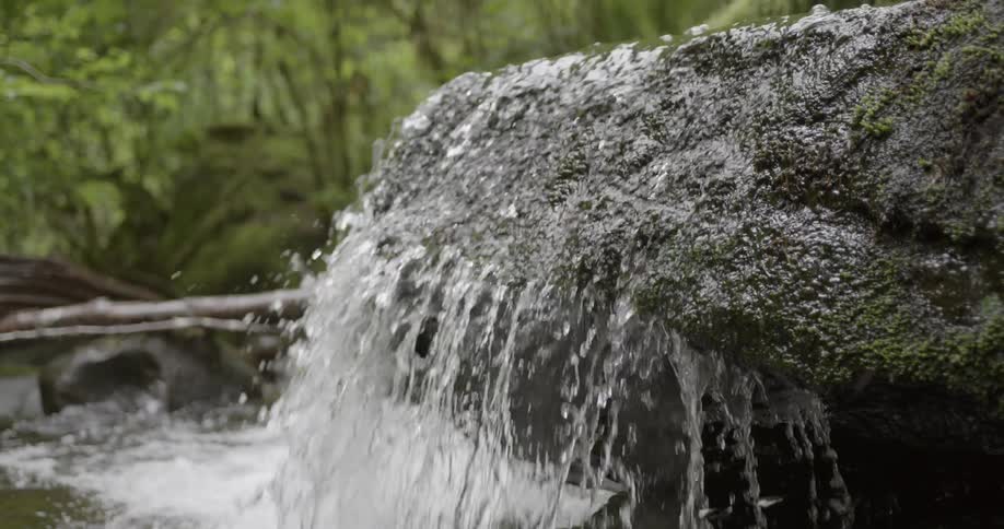 Close up of water from a brook flowing over a rock and splashing down below