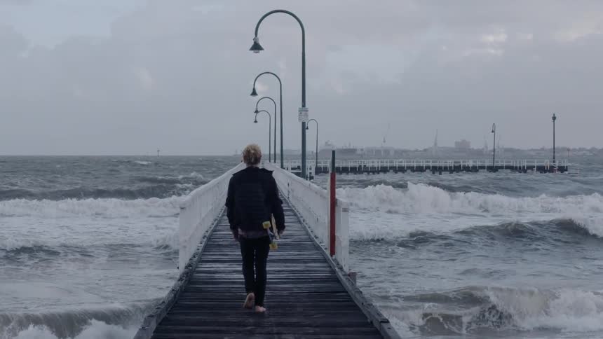 Woman walks down a pier carrying a skateboard