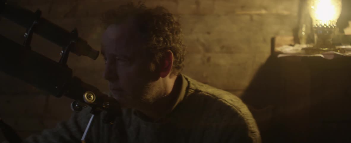 Man leans forward to look through a telescope