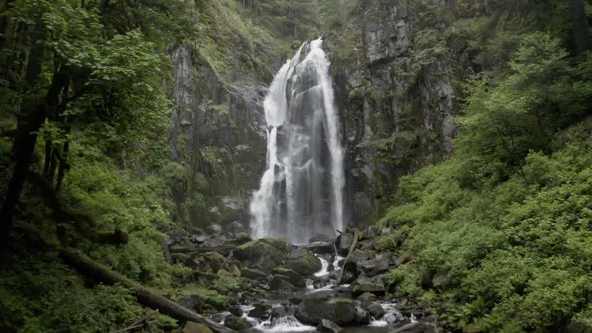 Aerial shot of a cascade flowing over a cliff into a rocky stream below