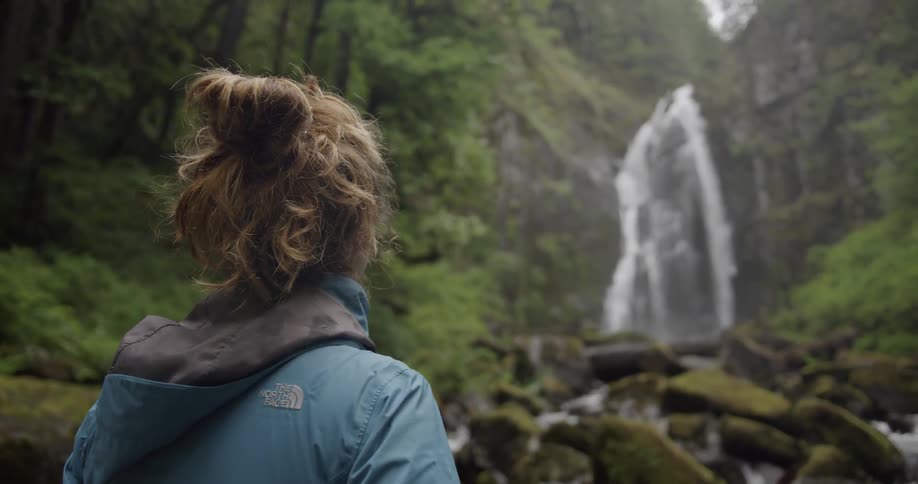 Woman stands in nature staring at a waterfall
