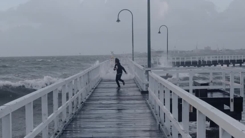 Boy runs from crashing waves on an ocean pier
