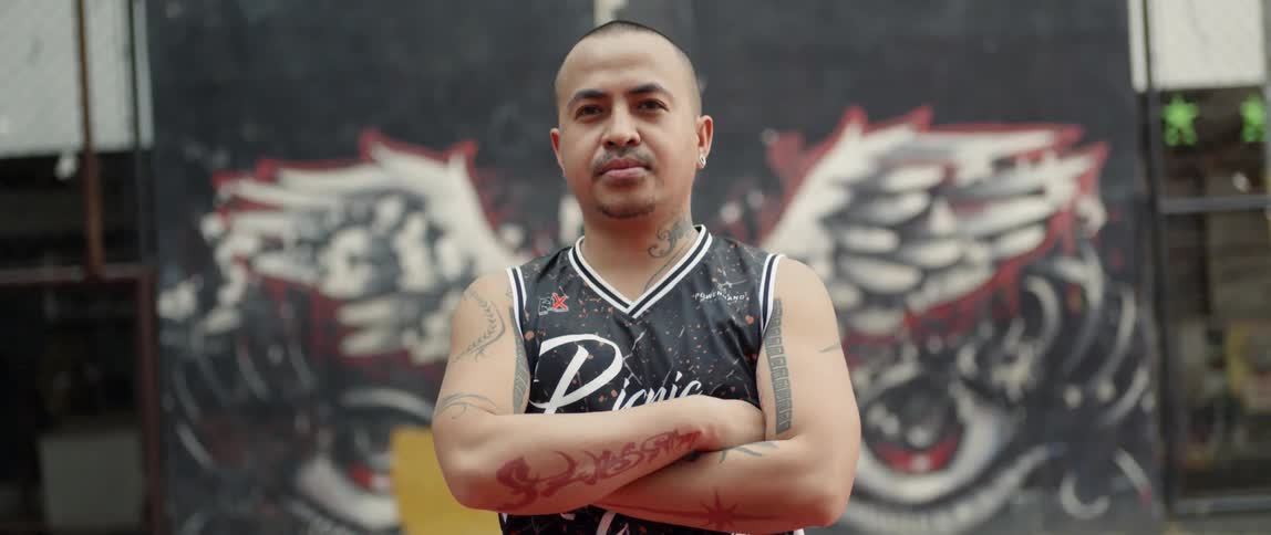 A man stands in front of graffiti with his arms folded
