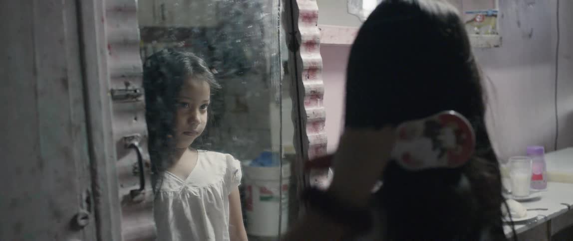 A girl brushes her long hair while looking in the mirror