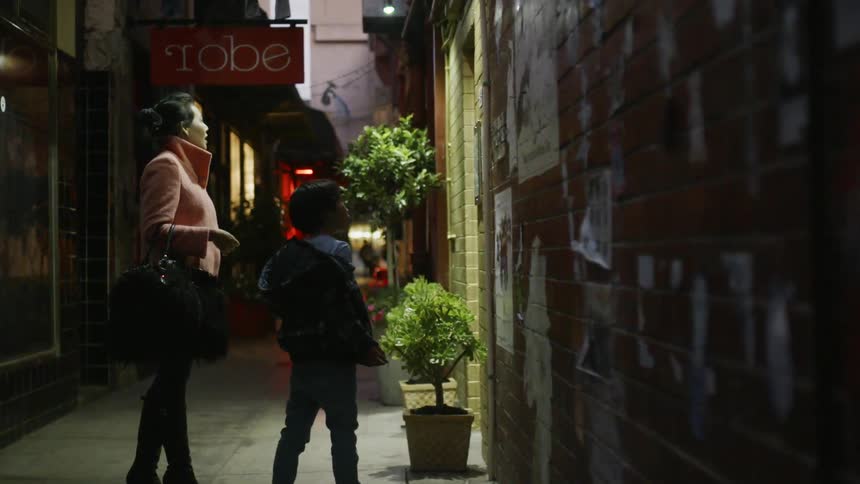 Woman and child stand in an alleyway of a city looking into a window