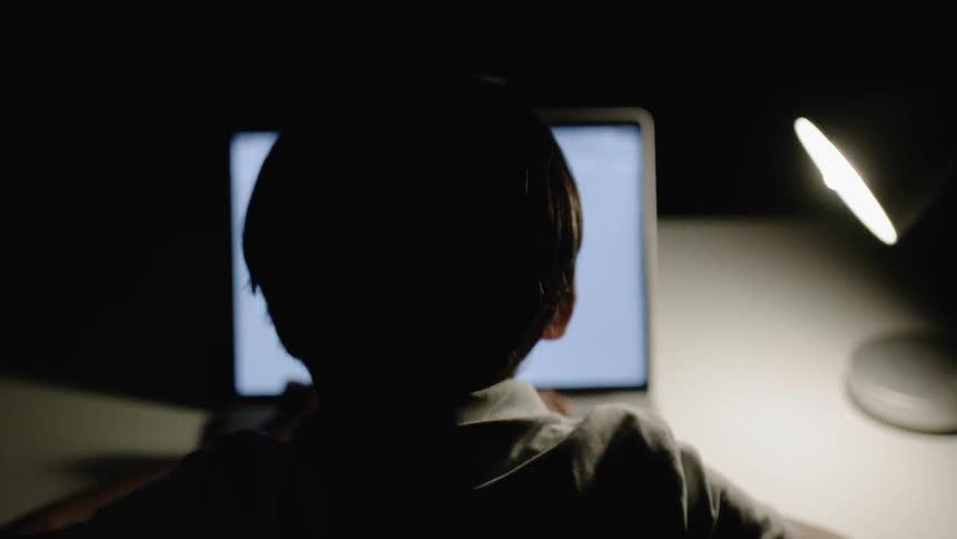 Child sits at a table typing on a laptop with a light shining on it