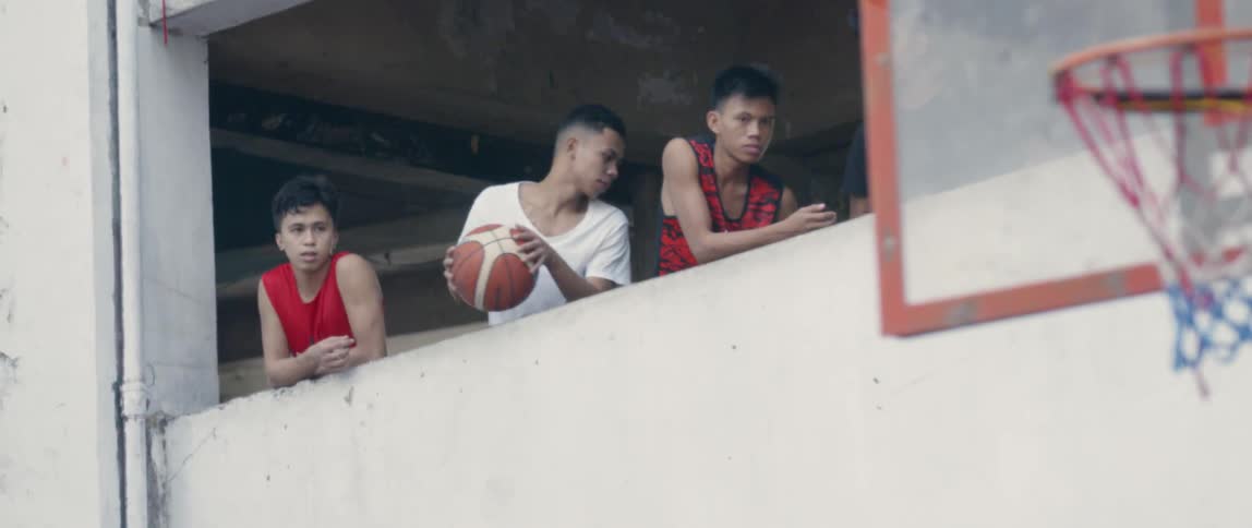 A boy holding a basketball leans over a balcony wall with two friends