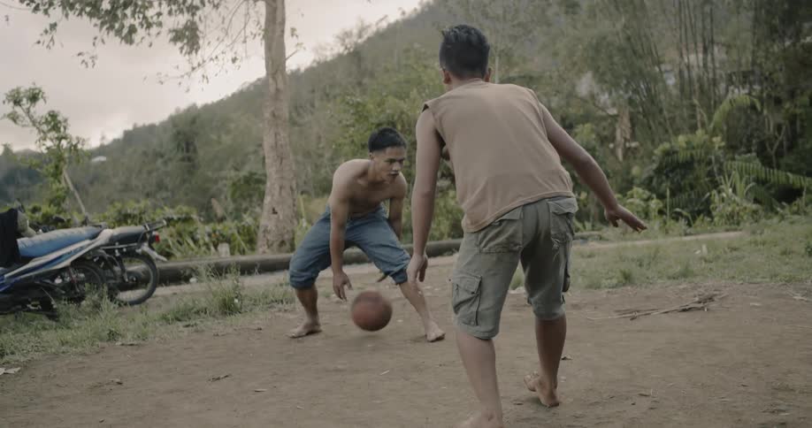 Teenagers play basketball on dirt