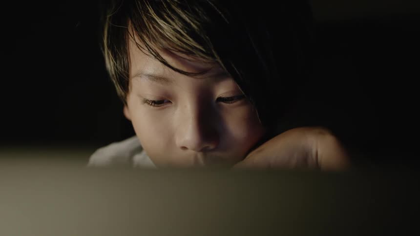 Young boy rests his head on his hand as he looks at a laptop