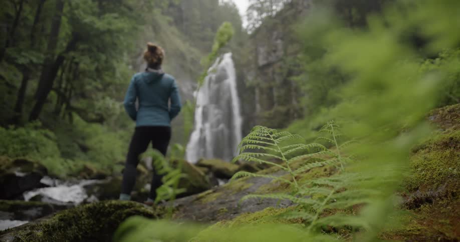 Rack focus shot of a woman staring at a cascade in a flourishing forest
