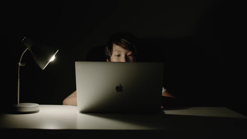 Young boy works on a laptop under the light of a lamp