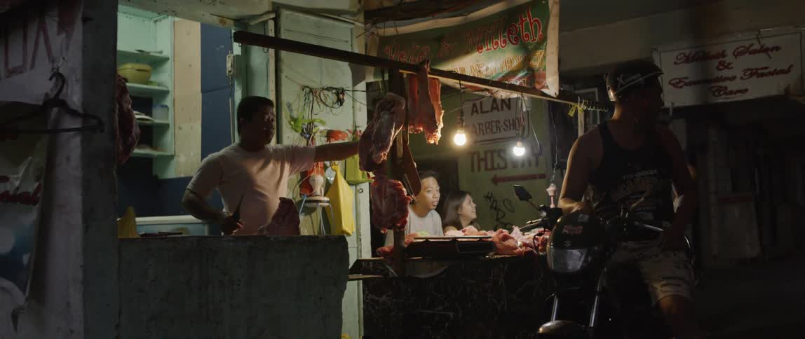 Men and women stand by a counter filled with meat and one person sits on a motorbike