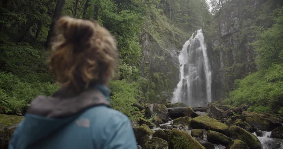 Woman watches a waterfall as she stands near the rocks