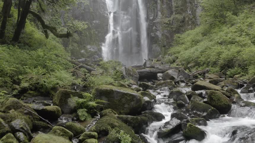 Push in shot of a waterfall in a lush forest flowing over a cliff