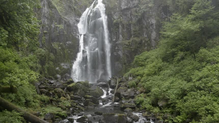 Pull out shot of a cascade flowing down a cliff into a creek below