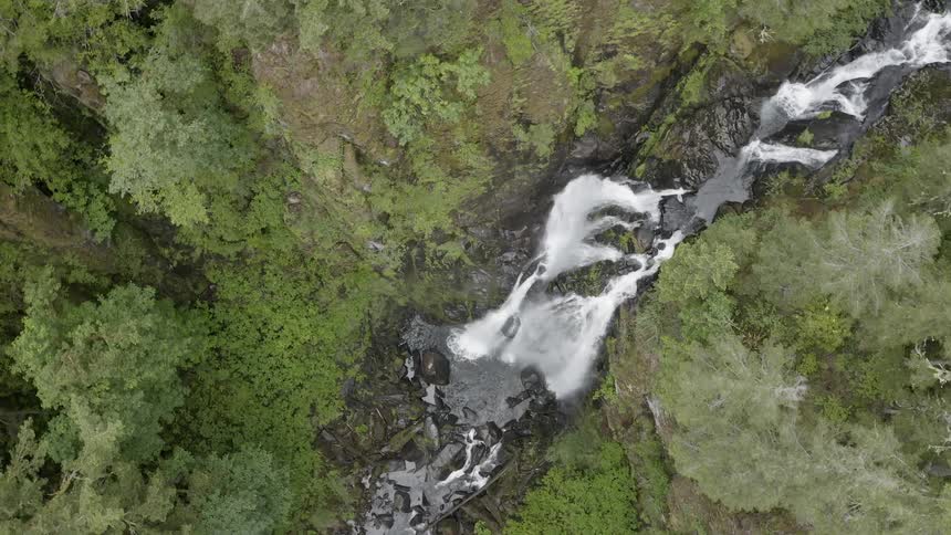 Spinning Aerial shot of a cascade rushing over a cliff in a green forest