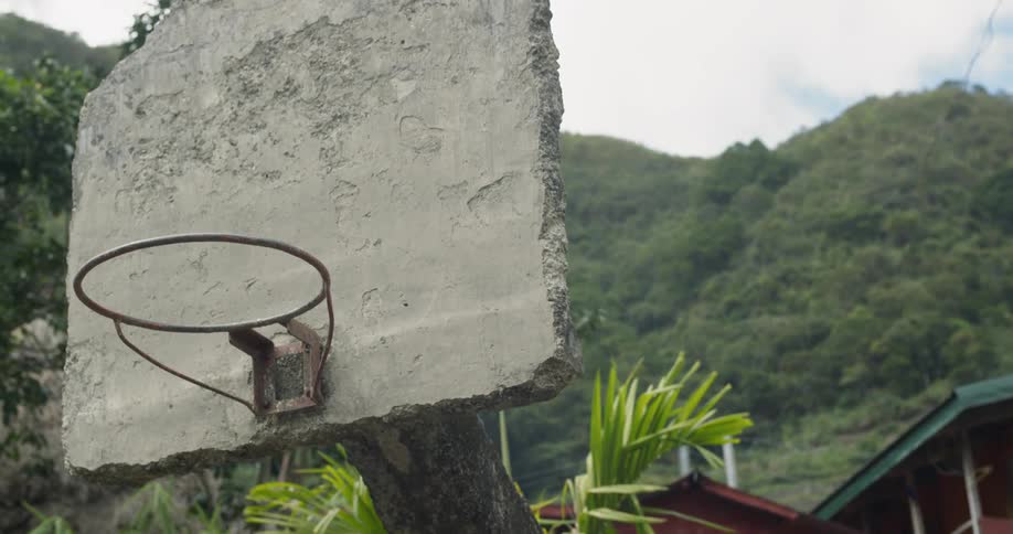 Old stone basketball hoop near trees and hills