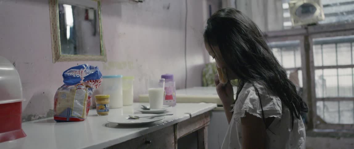 Young girl eats a sandwich as she sits at a table
