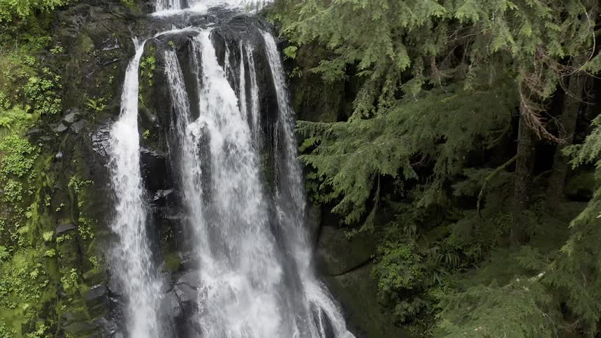Aerial shot of a cascade in a green forest flowing over a cliff