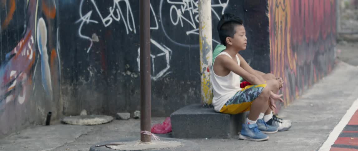 Children sit by a pole near the wall