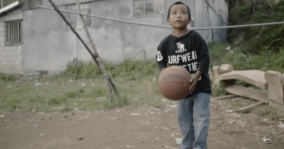 A boy dribbles a basketball in the dirt and then shoots