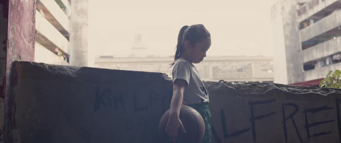 Child stands outside holding a basketball and looking down