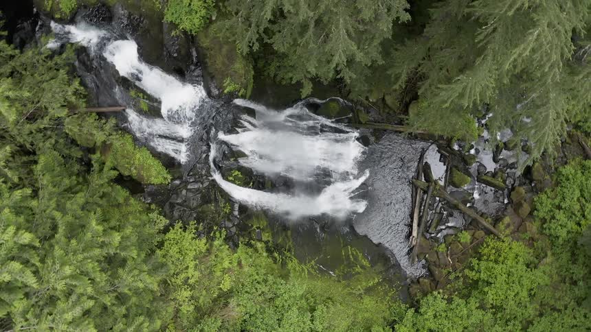 Spinning aerial shot of a waterfall in a lush forest rushing over a cliff into a brook below