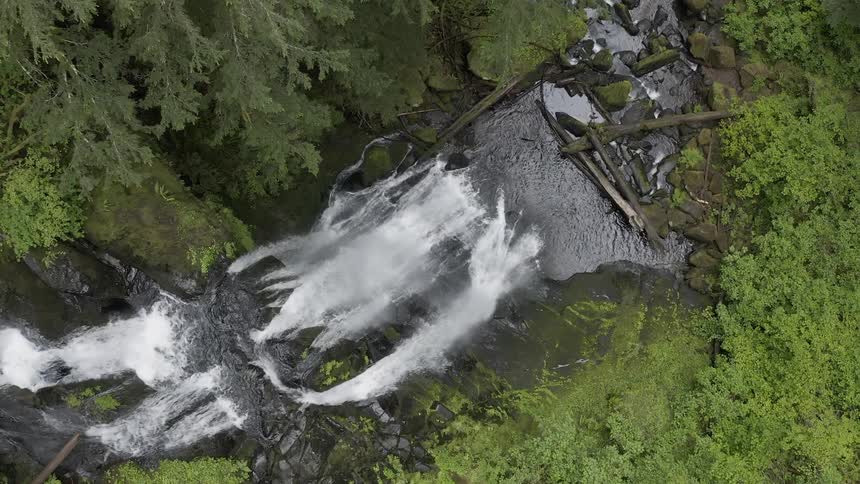 Birds-eye view of a waterfall in a lush forest falling into a rocky creek below