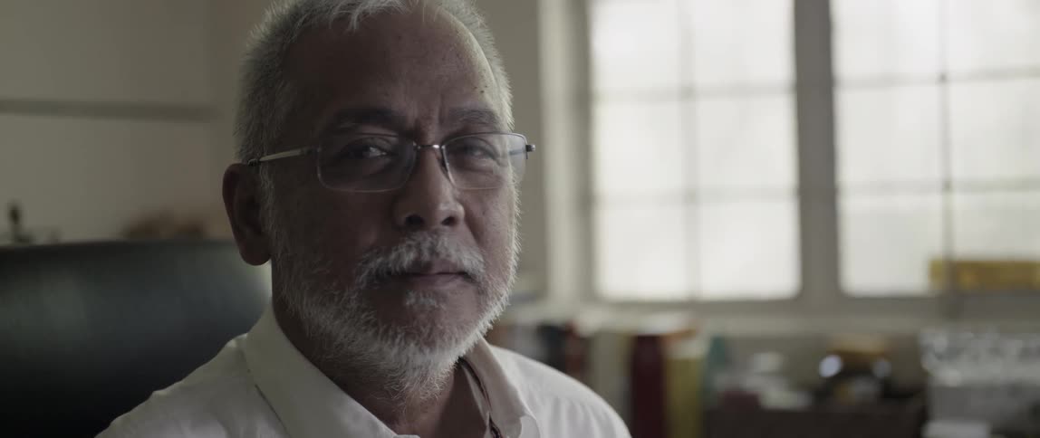 Elderly man sits blinking in front of a window