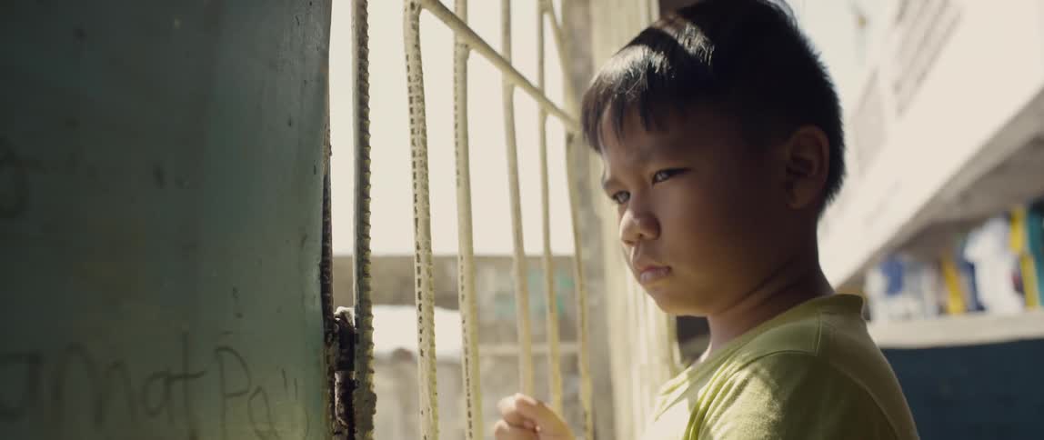 A child looks out through the bars on a sunny day
