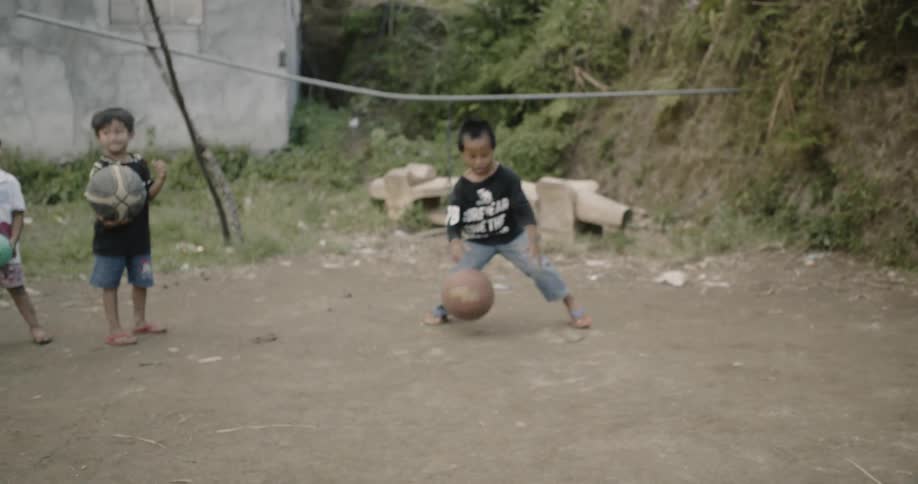 A boy catches a basketball and shoots at the hoop on a dirt road