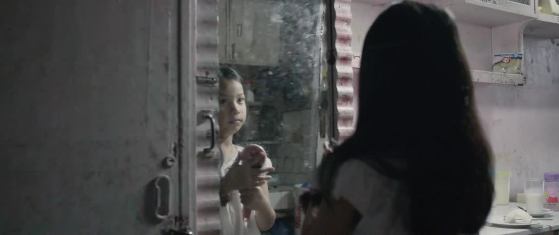 Young girl brushes her long hair as she looks in a mirror