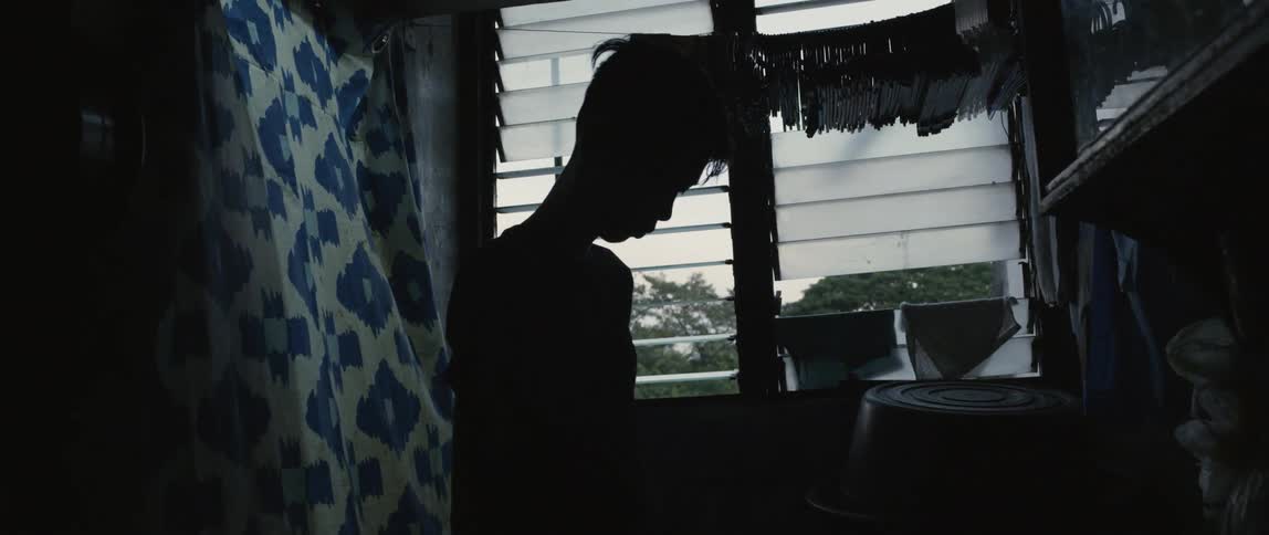 A child sits in the dark by the window