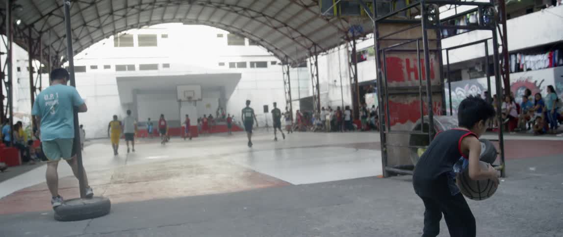 People watch boys play basketball on an outdoor court